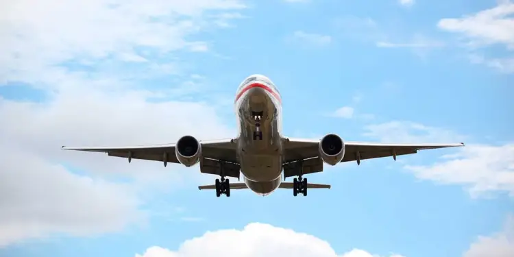 Vista frontal de un avión comercial en pleno vuelo con el tren de aterrizaje desplegado sobre un cielo nublado.