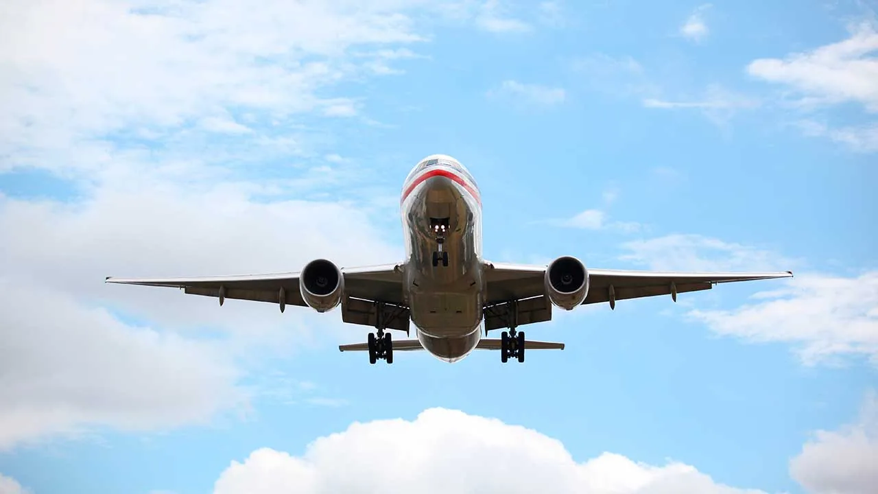 Vista frontal de un avión comercial en pleno vuelo con el tren de aterrizaje desplegado sobre un cielo nublado.